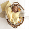 Newborn baby wrapped in a SNUGGLE HUNNY Organic Muslin Swaddle -  Sunlight with floral headband in a woven basket on a white background