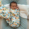 Newborn baby wrapped in a SNUGGLE HUNNY Organic Jersey Wrap - Citrus Squeeze, lying on a textured blanket in a woven basket.